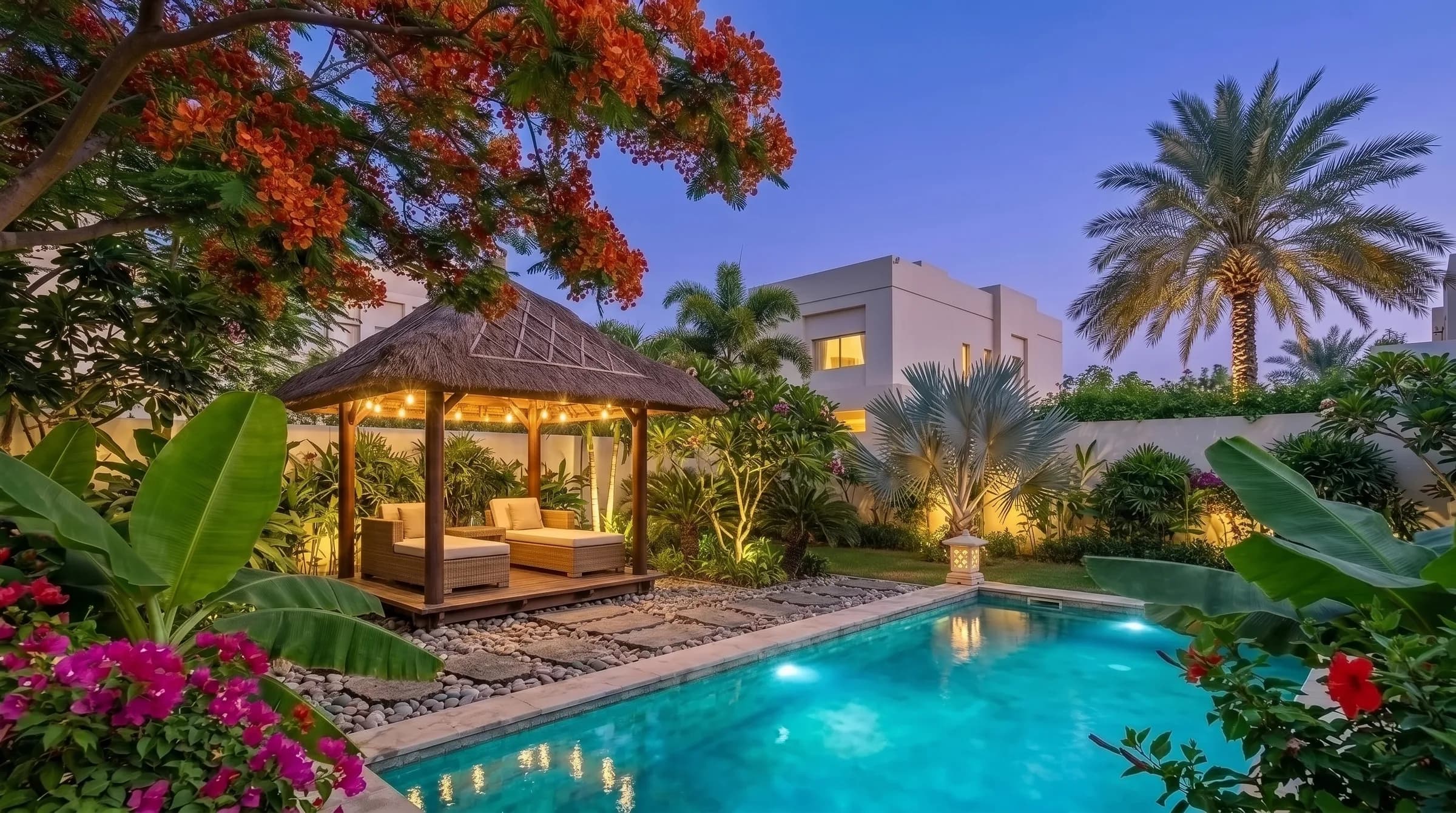 Tropical Dubai villa garden at blue hour: uplit palms and frangipani, string lights over a timber gazebo beside a glowing plunge pool